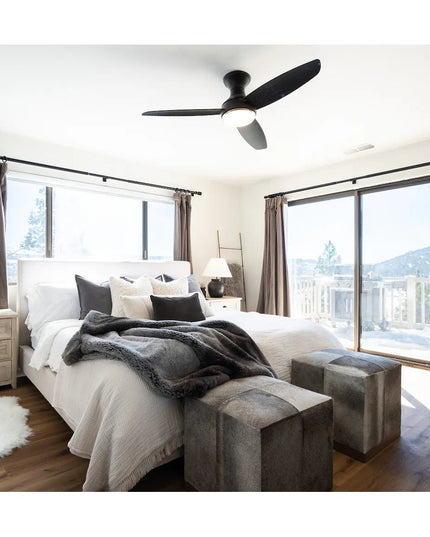 Modern bedroom with black ceiling fan, white bedding, gray throw blanket, wooden nightstand, and large windows with brown ...