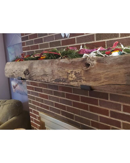 Rustic weathered wood beam mounted on brick fireplace wall using black steel J shelf brackets, decorated with Christmas gr...