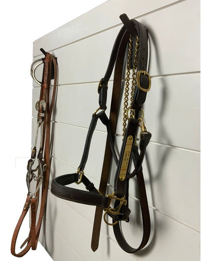 Black wall-mounted metal hooks holding leather horse bridles and tack equipment against white shiplap wall - The Tator Wal...