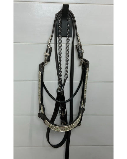 Black leather horse bridle with silver decorative chain accents hanging on white wall-mounted hook by Industrial Farm Co