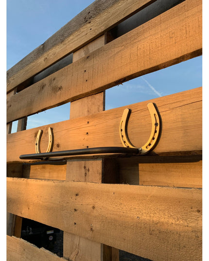Rustic golden horseshoe towel bar with black metal rod mounted on weathered wood fence, The Donahue by Industrial Farm Co