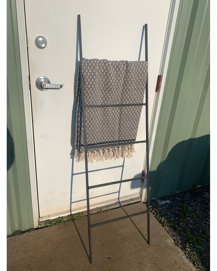 Black metal decorative ladder with geometric patterned throw blanket displayed outdoors against white door - The Lynn Meta...