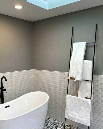 Black metal ladder towel rack by Industrial Farm Co displayed in modern bathroom with white subway tile and freestanding tub
