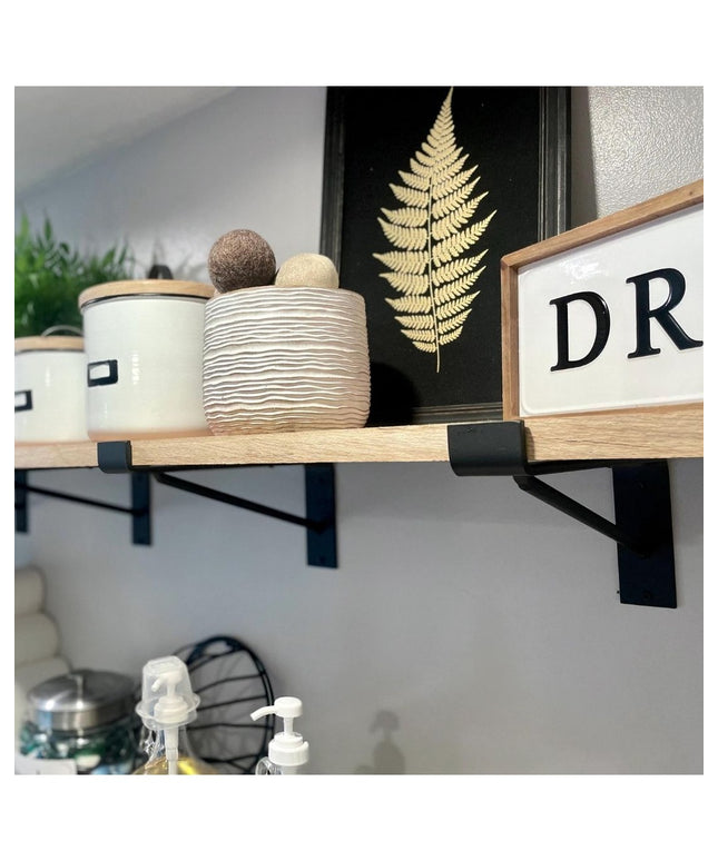 Black metal Nauseef shelf support brackets holding natural wood floating shelf with decorative items and fern artwork