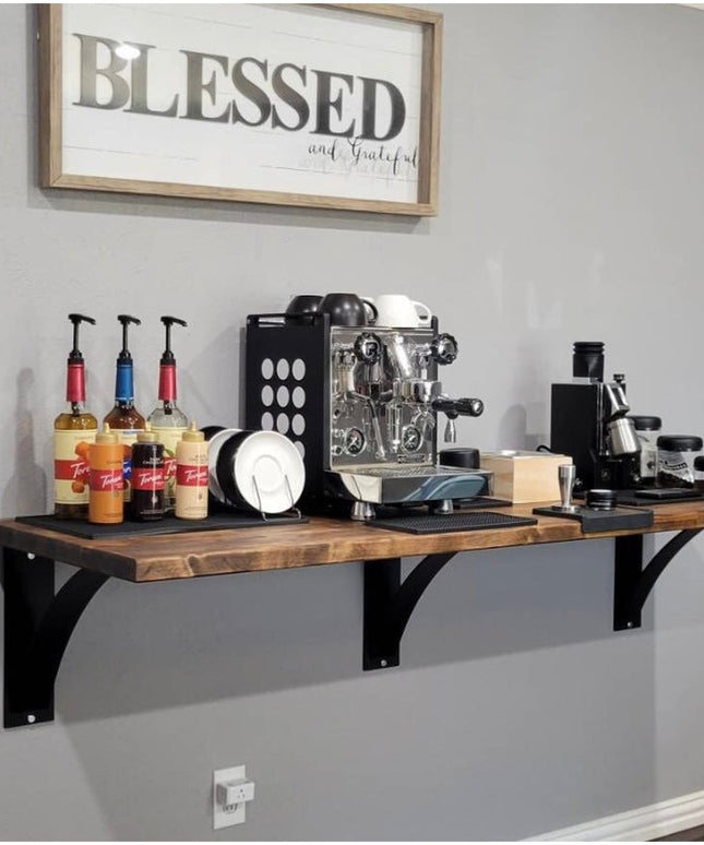 Industrial black metal shelf brackets supporting wood coffee bar with espresso machine and syrups on gray wall under Bless...
