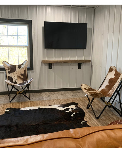 Black metal Rosamond shelf supports by Industrial Farm Co mounted on white wall holding rustic wood shelf below mounted TV...