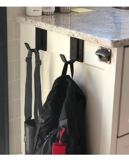 Black Dublin Mudroom Hook by Industrial Farm Co mounted on white kitchen cabinet door holding backpack and straps