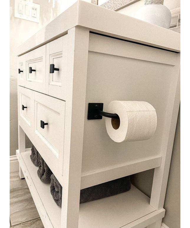 The Mitz black metal toilet paper holder by Industrial Farm Co mounted on white farmhouse bathroom vanity with open shelving