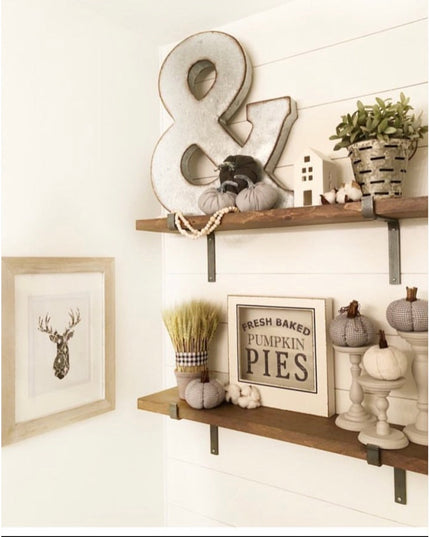 Black metal Z-style shelf brackets supporting rustic wood shelves with fall decor including pumpkins, wheat bundles, and "...