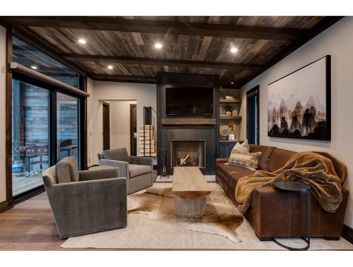 The Toby Firewood Holder by Industrial Farm Co displayed in modern rustic living room with exposed wood beams, stone firep...