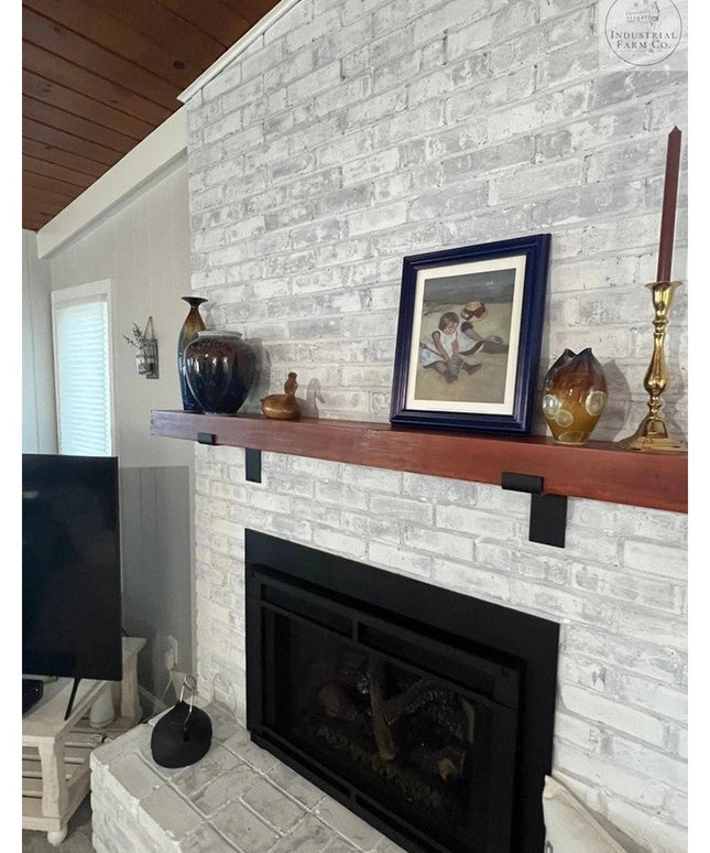 Black metal Z-style shelf brackets supporting wood mantel above white brick fireplace by Industrial Farm Co, displaying ru...