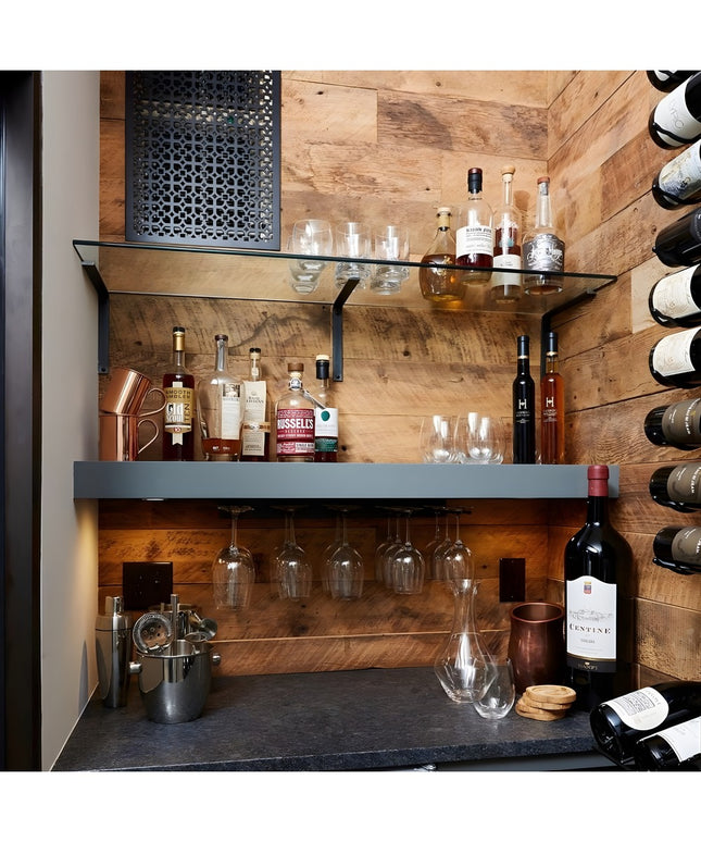 Modern home bar with black steel L-shaped shelf brackets supporting glass shelves, displaying liquor bottles and glassware...