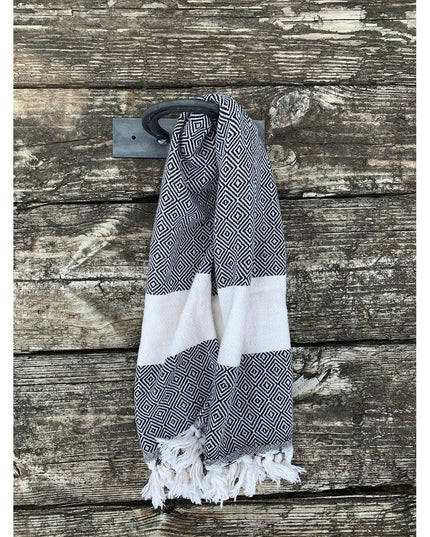 Black horseshoe towel holder mounted on weathered wood wall with geometric patterned hand towel featuring white tassels - ...