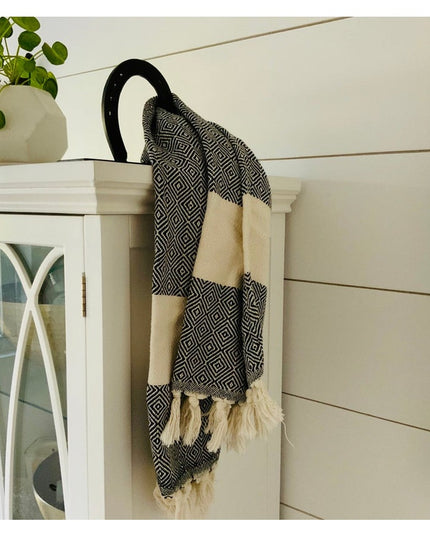 Black horseshoe-shaped wall mount towel holder by Industrial Farm Co displaying patterned towel with tassels on white cabinet