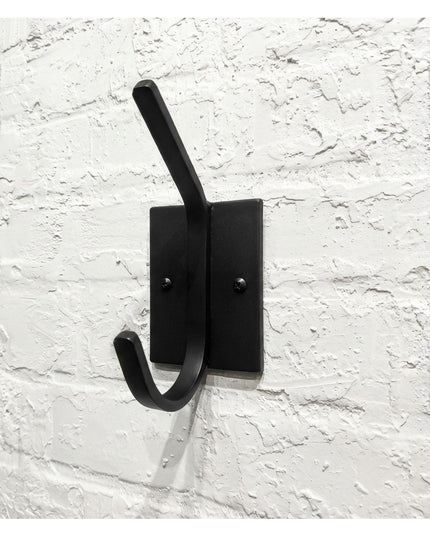 Black metal Felix Wall Hook by Industrial Farm Co mounted on white painted brick wall, featuring minimalist design with si...