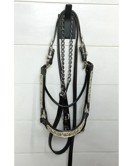 Black leather horse bridle with silver decorative elements and chain detailing hanging on white wall-mounted hook by Indus...