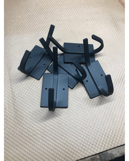 Black metal Felix wall hooks by Industrial Farm Co scattered on white textured surface, showing rectangular mounting plate...