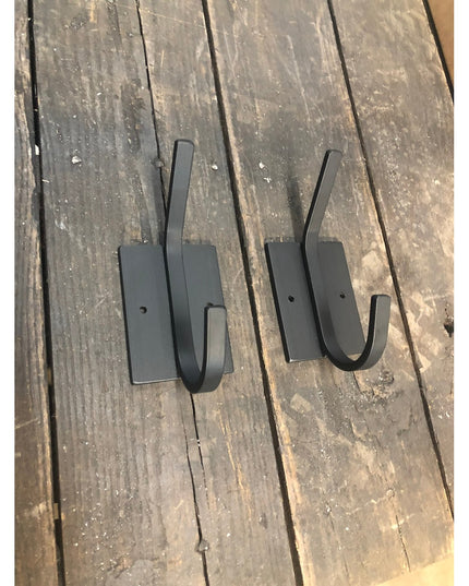 Two black metal Felix Wall Hooks by Industrial Farm Co displayed on weathered wood planks, featuring curved hooks with rec...