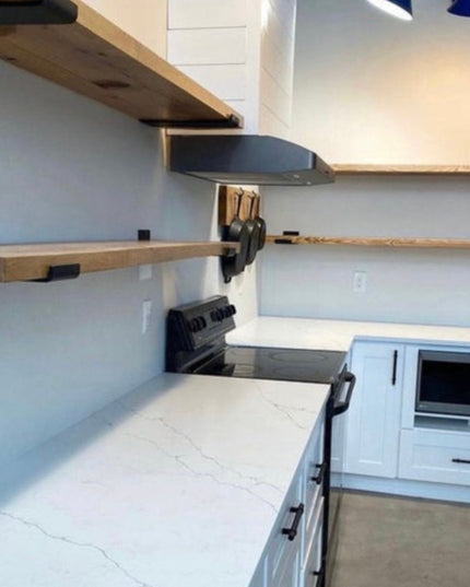 Black steel J-bracket shelf supports holding natural wood floating shelves in modern white kitchen with Industrial Farm Co...