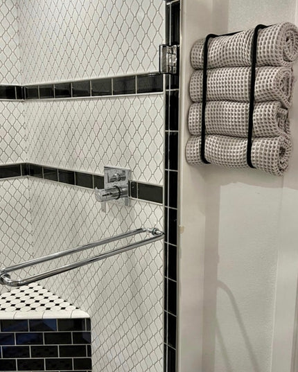 Black metal Tyler bathroom towel rack by Industrial Farm Co mounted on white door holding rolled waffle weave towels in mo...