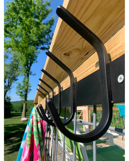 Black metal Eastman Coat & Hook Rack mounted under wooden pergola with colorful towel hanging, showing curved hook design
