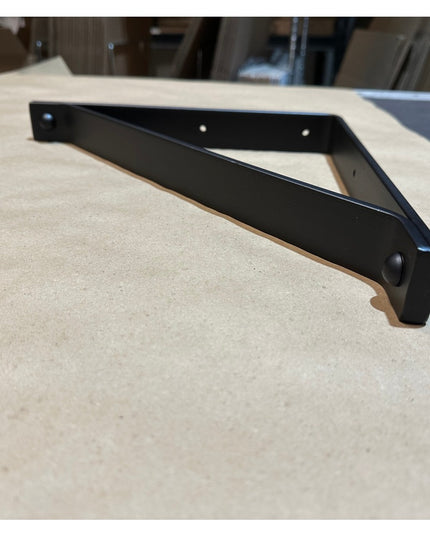 Black metal triangular Joyce Modern Shelf Support bracket by Industrial Farm Co displayed on light wood surface showing sl...