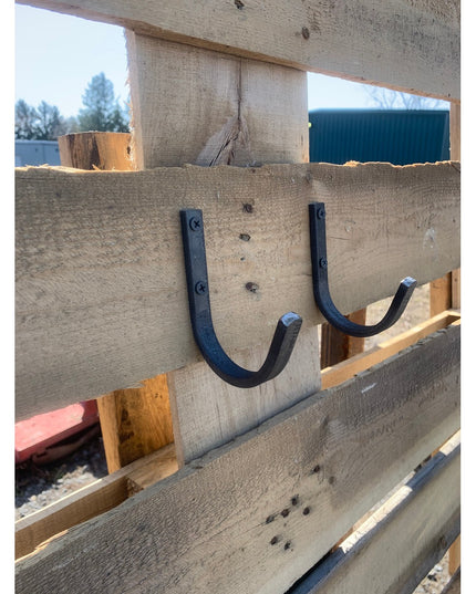Two black metal Kenny wall hooks mounted on weathered wood beam, showing curved U-shaped design with visible screws from I...