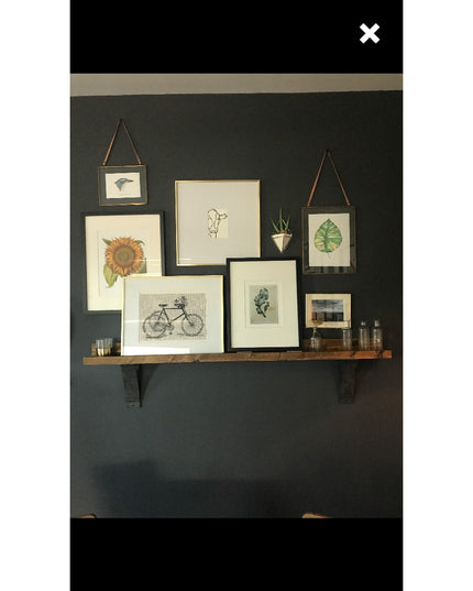 Rustic wooden shelf with black Jeffery Style Shelf Brackets by Industrial Farm Co displaying framed botanical and vintage ...