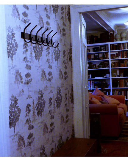 Black metal Eastman Coat & Hook Rack mounted on floral wallpaper wall next to built-in bookshelf and orange armchair