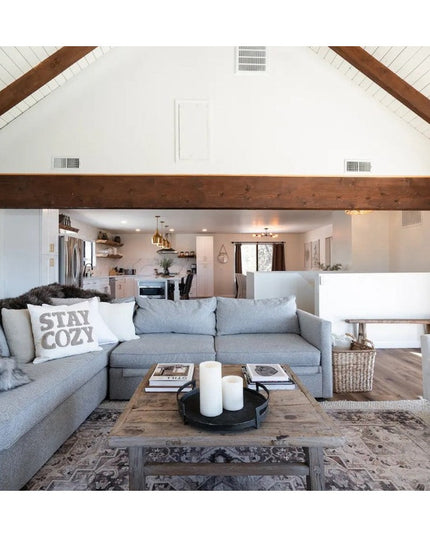 Modern rustic living room with exposed wood beams, gray sectional sofa, and wooden coffee table featuring cozy farmhouse d...