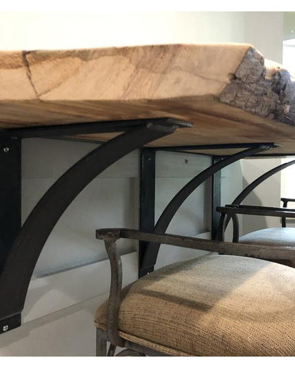 Black metal Lexica 4 inch wide curved shelf brackets supporting rustic wood countertop with bar stools underneath by Indus...