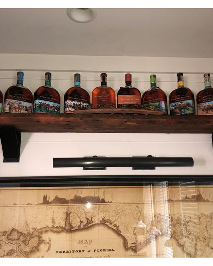 Rustic wooden shelf with black metal brackets displaying bourbon whiskey bottles above framed vintage Florida territory map