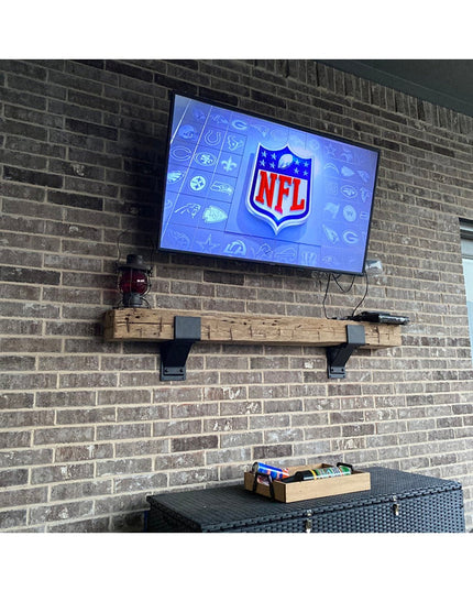 Rustic wood floating shelf with black metal Monroe Style Corbel Brackets mounted on brick wall under mounted TV displaying...