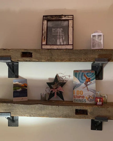 Rustic wooden floating shelves with black metal brackets mounted on beige wall, displaying decorative items and books in f...