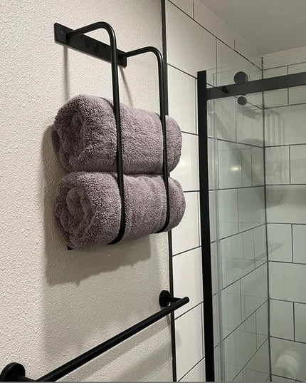 Black metal Tyler Bathroom Towel Rack by Industrial Farm Co mounted on white bathroom wall holding gray towels next to gla...
