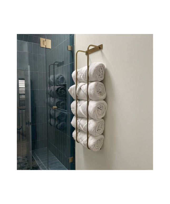Brass wall-mounted Tyler Bathroom Towel Rack by Industrial Farm Co holding rolled white towels next to modern glass shower...