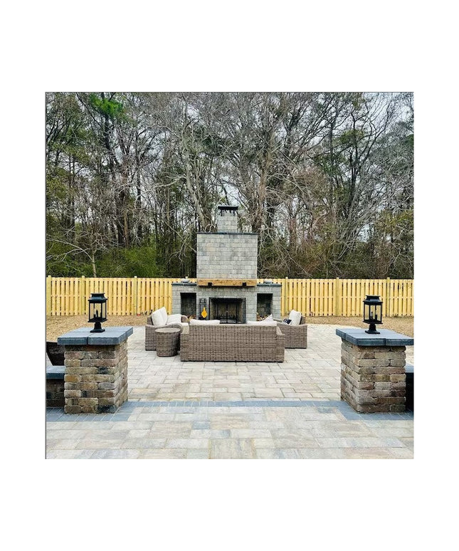 Rustic outdoor patio with stone fireplace, wicker furniture, and black lanterns on stone pillars with paver flooring and w...