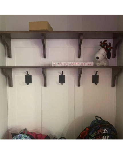 Black metal Felix wall hooks mounted on white wood cubbies with dark brackets, featuring Christmas decor and bags below fr...
