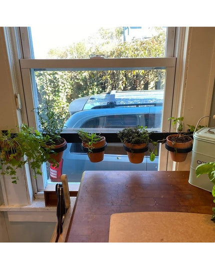 The Yonkers Horizontal Steel Planter by Industrial Farm Co holding terracotta pots with herbs on kitchen windowsill