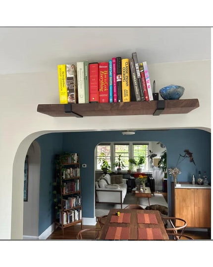 Dark wood floating shelf with black metal J-bracket supports holding colorful books, installed above arched doorway in mod...