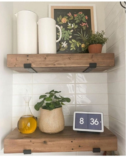 Black metal J-style shelf brackets supporting rustic wood floating shelves with white ceramic pitchers, botanical print, a...