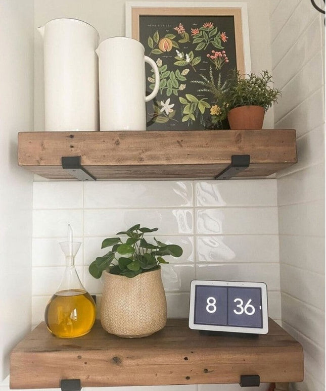 Black metal J-style shelf brackets supporting rustic wood floating shelves with white ceramic pitchers, botanical print, a...