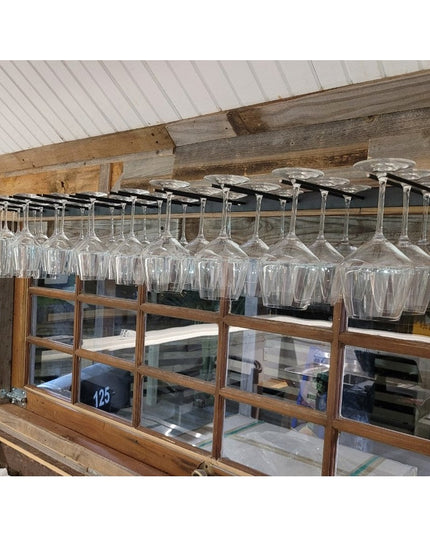 White Plains Wine Glass Rack by Industrial Farm Co mounted under rustic wooden beams holding multiple wine glasses in mode...