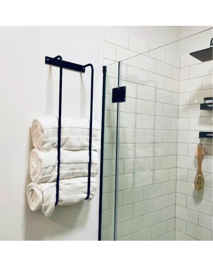 Black metal Tyler Bathroom Towel Rack by Industrial Farm Co mounted on white wall holding white towels next to glass showe...