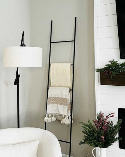 Black metal decorative ladder The Lynn by Industrial Farm Co displaying cream blankets in modern living room with fireplace