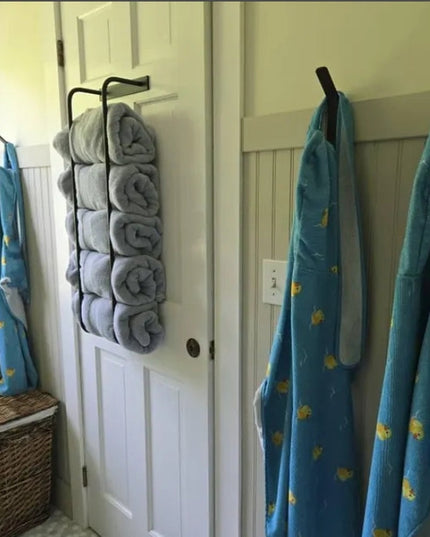 Black metal Tyler Bathroom Towel Rack by Industrial Farm Co mounted on white door holding rolled gray towels with blue pat...