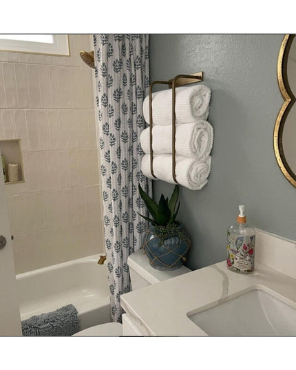 Gold brass Tyler Bathroom Towel Rack by Industrial Farm Co mounted on gray wall holding white rolled towels in modern bath...