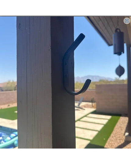 Black metal Henrietta 1" Wide Double Hook by Industrial Farm Co mounted on wooden beam with desert landscape view in backg...