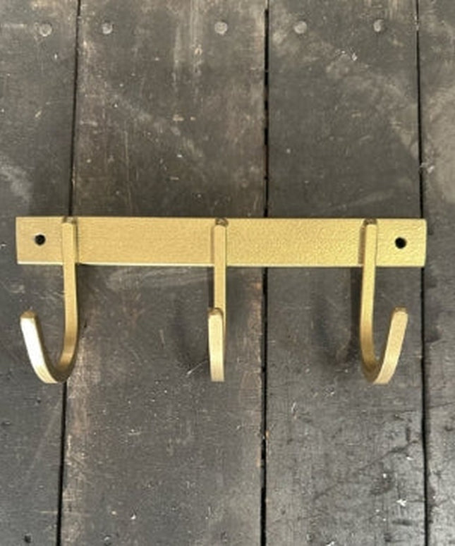 Rustic brass-colored metal key rack with three curved hooks mounted on weathered gray wooden planks background by Industri...