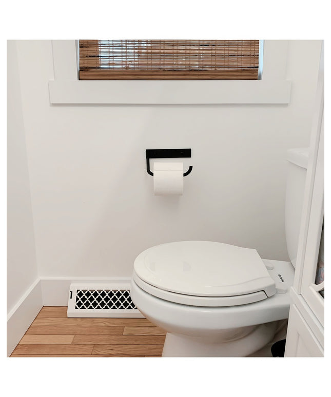 The Howlett Hill black metal toilet paper holder by Industrial Farm Co mounted on white bathroom wall with white toilet an...